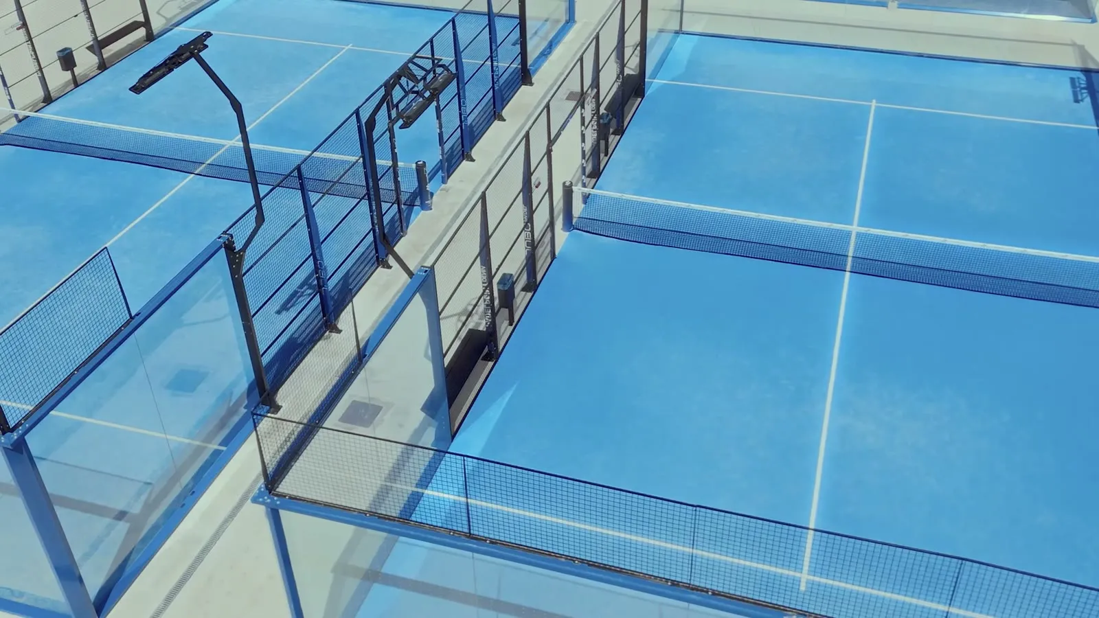 Zwei Panoramic Courts aus erhöhter Sicht: blaue Spielflächen, umlaufende Glaswände, schlanke Rahmen — eine Anlage, nicht ein einzelner Platz